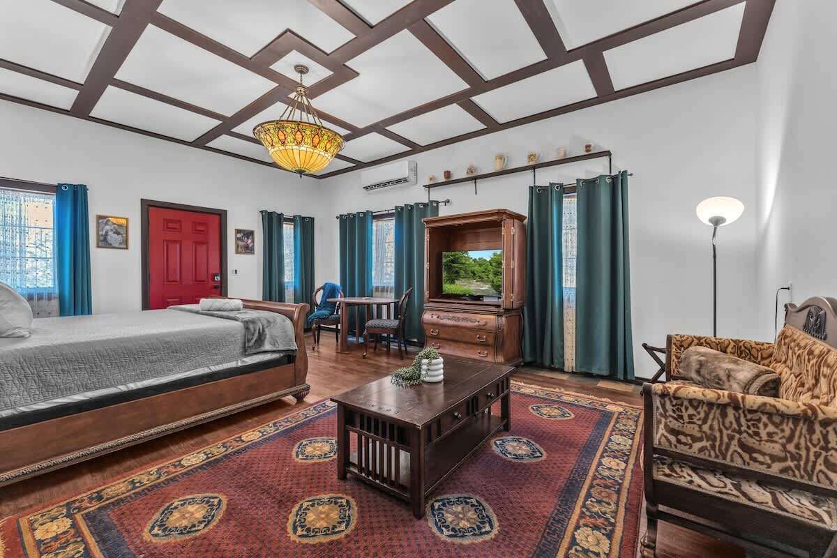 A spacious room with a bed, a sofa, a wooden coffee table, and a television.