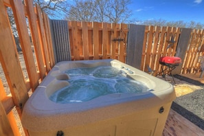 Ein Whirlpool in einer Außenanlage mit Holzzaun und Grill im Hintergrund.