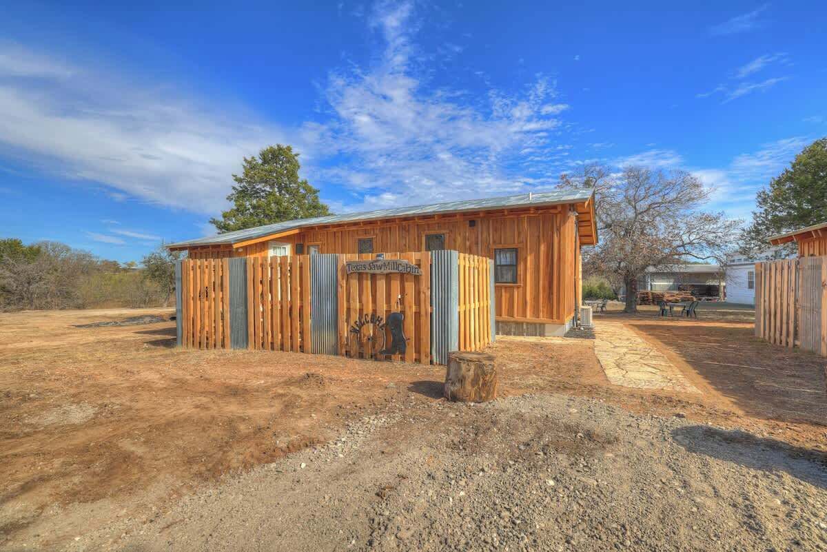 Un edificio in legno con un cancello in lamiera ondulata e un cartello con la scritta "Texas Saw Mill Cabin".