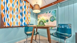 A dining area with a wooden table, two glass chairs, and a colorful abstract painting on the wall.