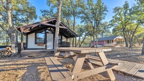 A rustic cabin with a wooden deck and picnic table, surrounded by trees.
