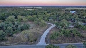 An aerial view of a rural landscape with a winding road, scattered trees, and a few buildings.