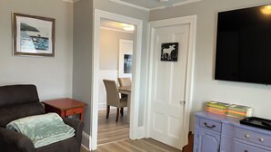 Un salon avec un canapé en cuir marron, une petite table en bois, un tapis à carreaux, une porte blanche ornée d’une image d’un élan et un téléviseur fixé au mur.