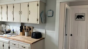 Une cuisine avec des armoires blanches, un plan de travail en bois et un grille-pain. On y trouve une porte sur laquelle est apposé un panneau représentant un ours.