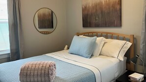 Un lit bien fait, avec une couette bleue, une tête de lit en bois et un miroir rond accroché au mur.