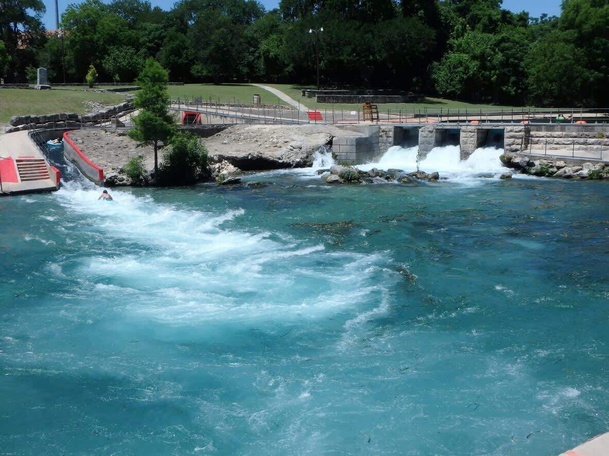 A water slide leading into a river with a bridge in the background.