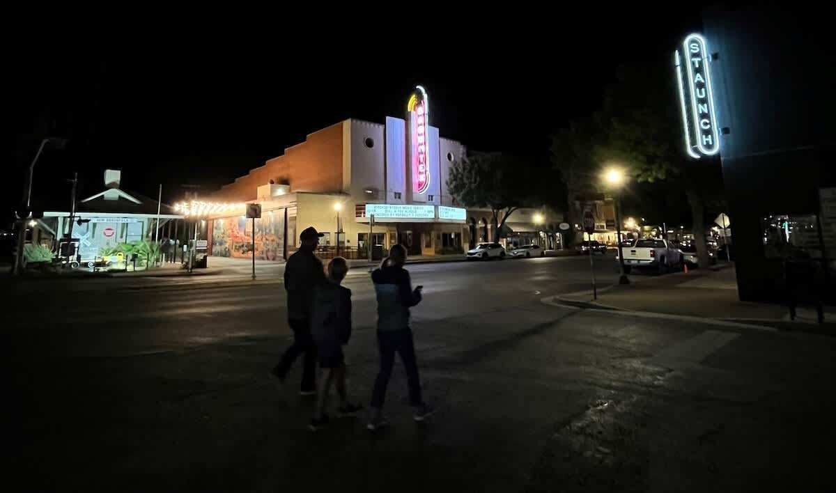 Un théâtre doté d’un auvent et d’une enseigne lumineuse, situé à un carrefour où passent des piétons.
