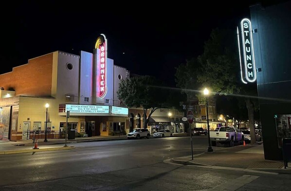 A street view at night with a theater and a store with illuminated signage.