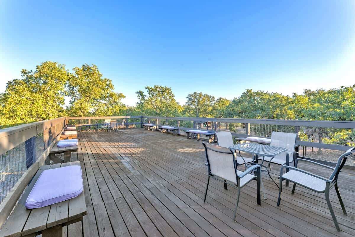 Une terrasse en bois avec des espaces de détente en plein air, comprenant des bancs et des tables, donnant sur un paysage naturel.