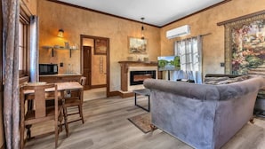 A cozy living room with a fireplace, a dining area with a wooden table and chairs, and a large painting on the wall. - The Vines Retreat, Hot-tubs, Game Room, 10-mins to Downtown! (Fredericksburg)