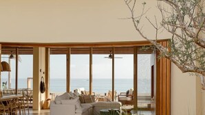 A spacious living area with a large sofa, a dining table, and chairs. There is a view of the sea through large windows. - Increíble casa frente a la playa (Ligth House Point States)