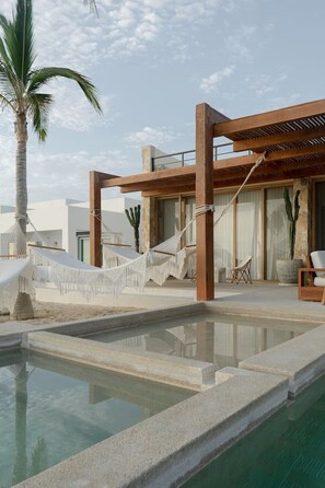 Un área de piscina con una hamaca, una palmera y una pérgola de madera.
