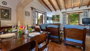 Un coin repas avec une table en bois dressée pour quatre personnes, un téléviseur et un tableau accroché au mur.