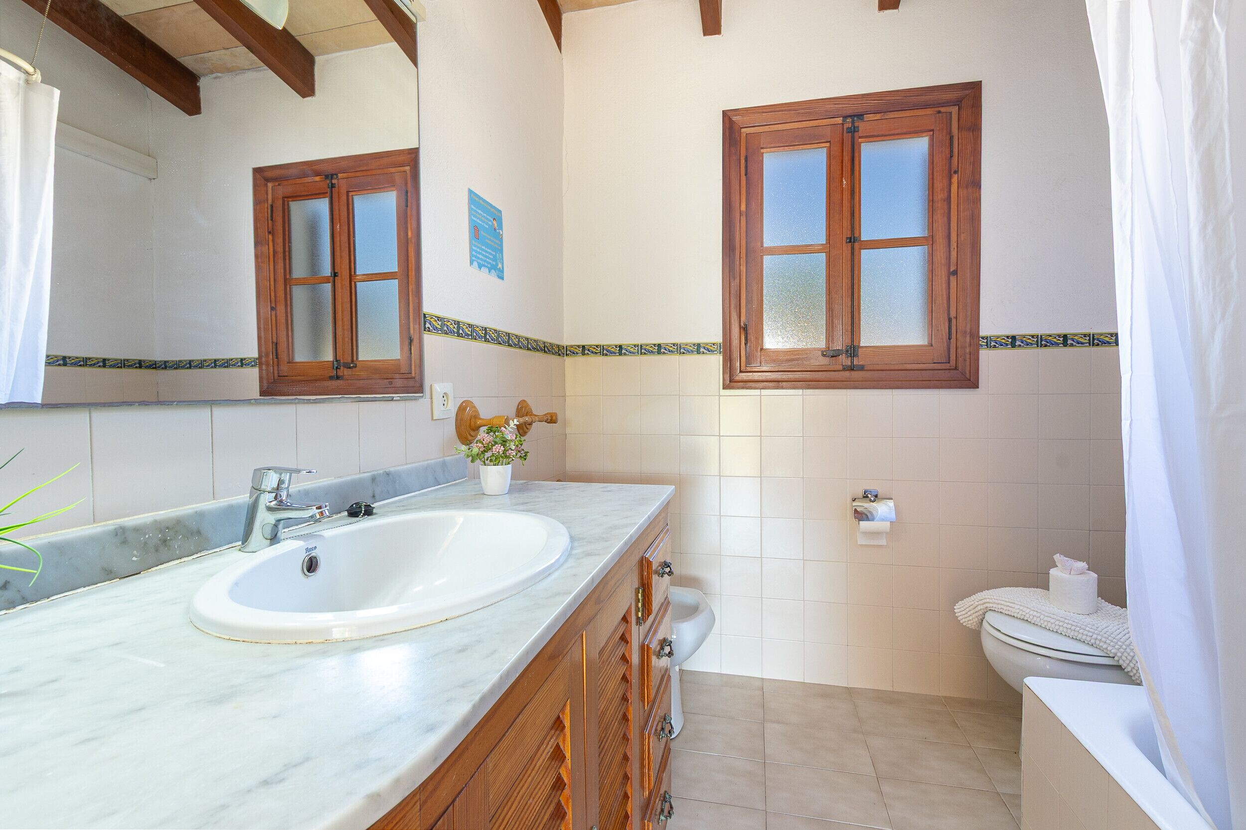 A bathroom with a marble sink, wooden cabinets, a toilet, and two windows with wooden frames.