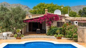 Un espace aménagé au bord de la piscine, comprenant une maison, du mobilier d’extérieur et des plantes en pot.