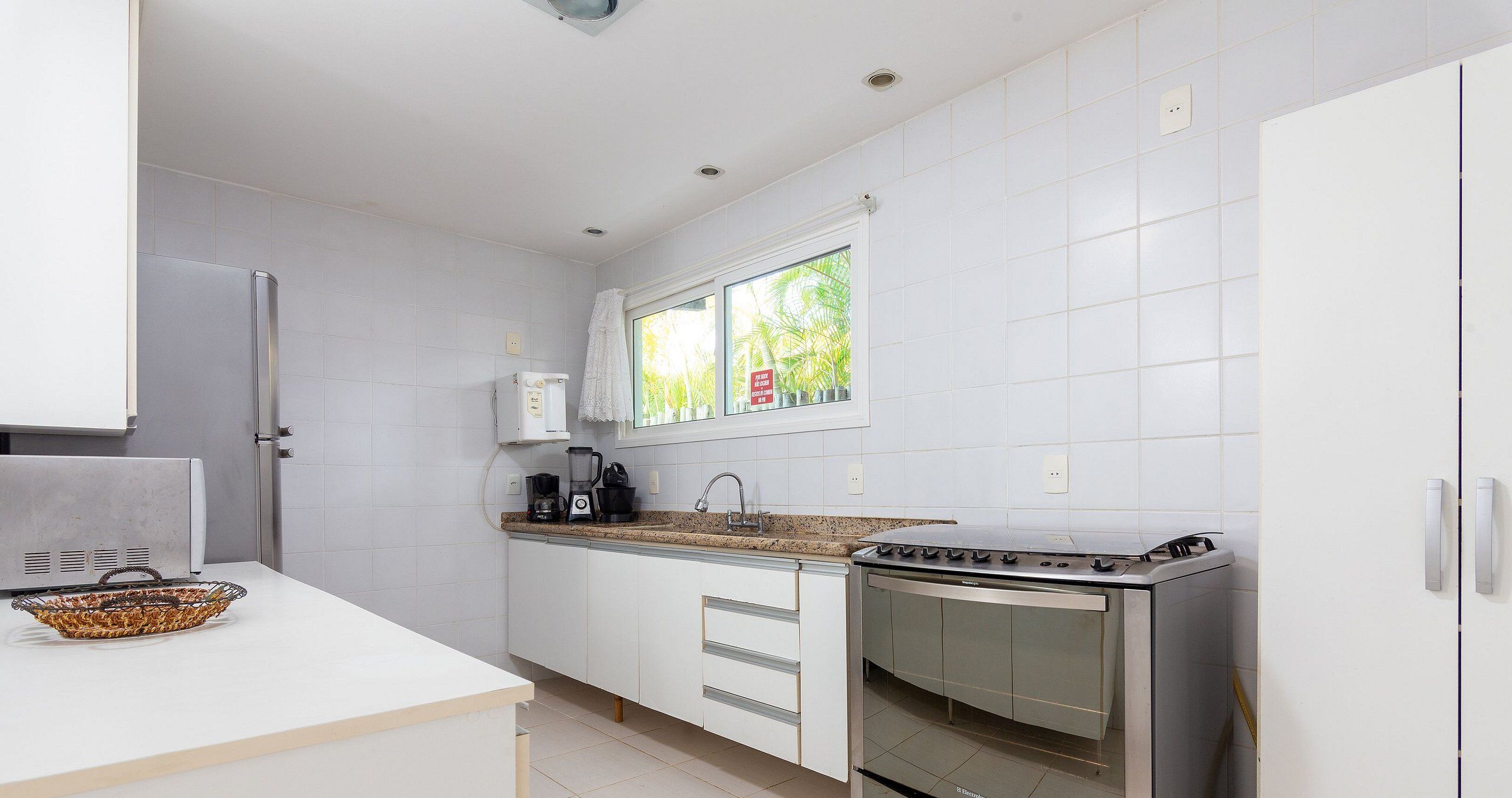 Une cuisine moderne avec des meubles blancs, un four encastré et une fenêtre donnant sur un paysage verdoyant.