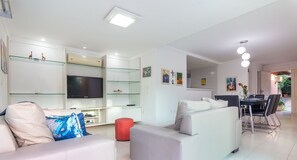 Una sala de estar moderna con sofá, televisor, estanterías de vidrio y un comedor.