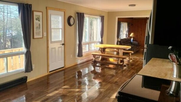 Una habitación con piso de madera, un banco de madera, una mesa y una ventana con cortinas.