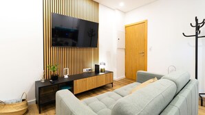 A modern living room with a flat-screen TV mounted on a wooden panel wall, a black entertainment unit, a grey sofa, and a wooden door.