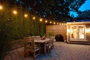 Eine Terrasse im Freien mit einem Holztisch und -stühlen, umgeben von einem Holzzaun und Lichterketten.