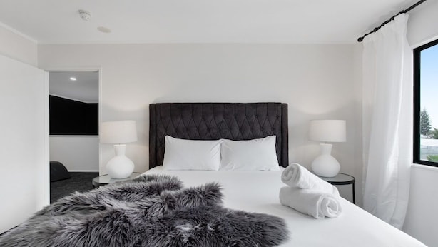 A modern hotel room with a large bed, two bedside lamps, a fluffy rug, and a view of the outdoors.