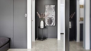 A hallway with a grey wall, a framed artwork, and a vase with flowers on a stand.