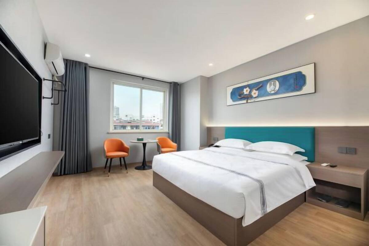 Camera d'albergo moderna con un letto grande, una scrivania, due sedie, una TV e una finestra con vista sulla città.