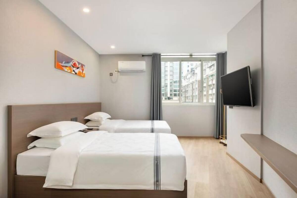 Camera d'albergo con due letti, una televisione a schermo piatto, un condizionatore d'aria e una finestra con tende.
