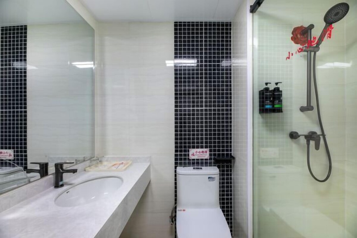 Ein Badezimmer mit einem weißen Waschbecken, schwarzen Fliesenwänden, einer Duschkabine aus Glas und einer Toilette.