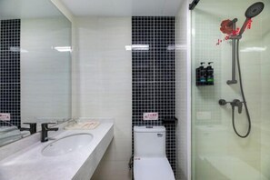 Un bagno con un lavandino bianco, pareti piastrellate di nero, cabina doccia in vetro e un water.