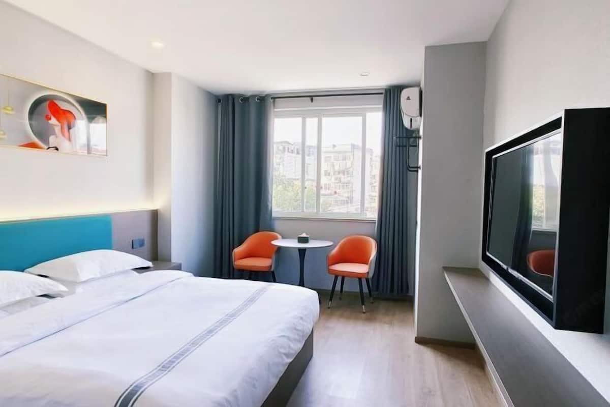 Una camera d'albergo con un letto, due sedie, una TV e una finestra con tende.