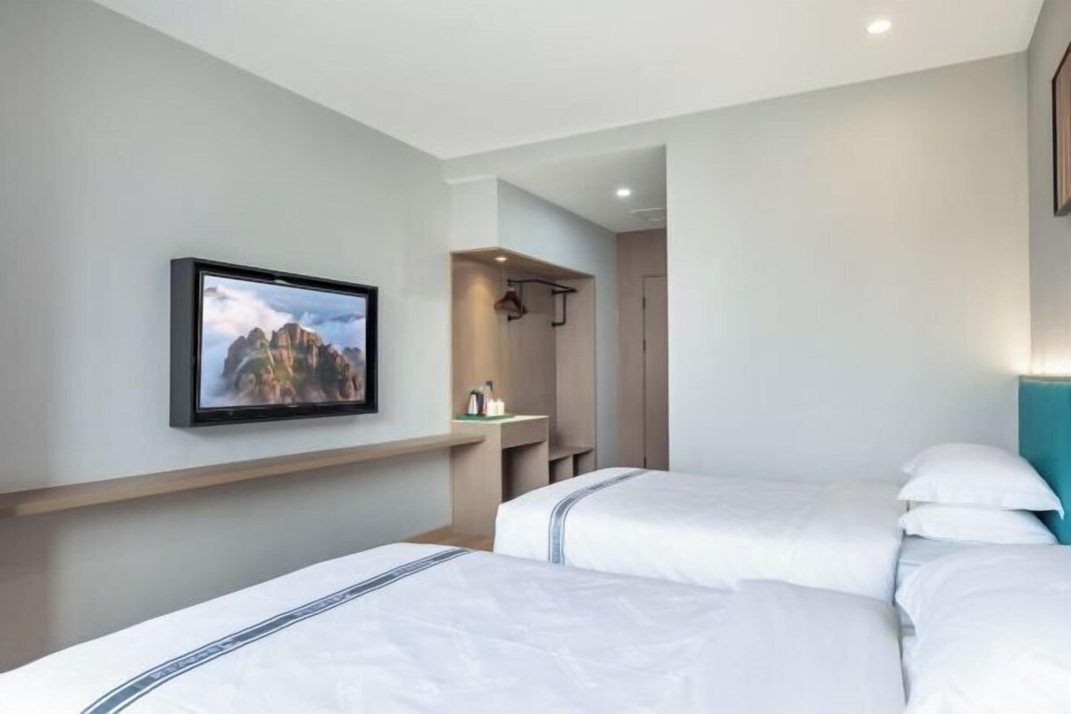 Ein modernes Hotelzimmer mit zwei Betten, einem Wand-Fernseher, einem kleinen Schreibtisch und einem begehbaren Kleiderschrank.