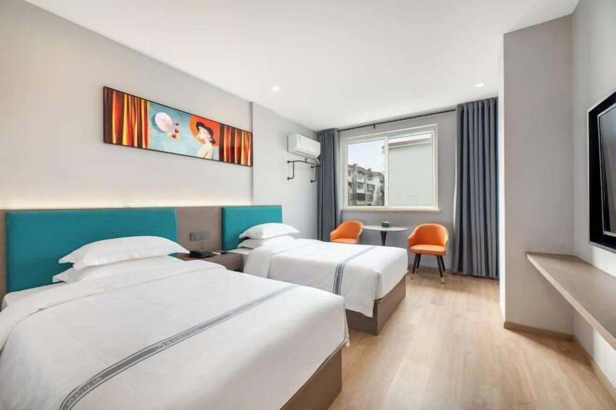 Una camera d'albergo con due letti, una finestra con tende, una TV e un quadro appeso al muro.