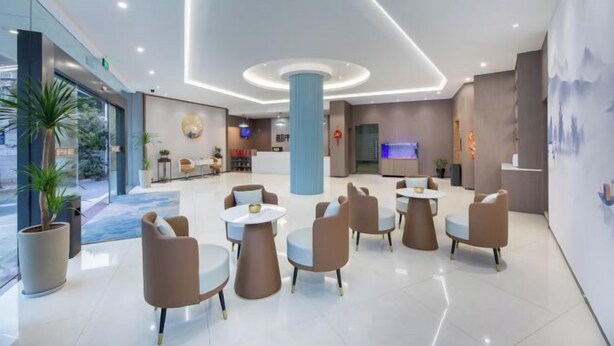 A modern hotel lobby with a central column, seating area, reception desk, and large windows. - City 118 Old Street Binjiang Road (Huangshan City)