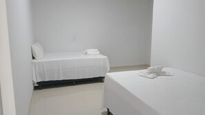 A small, clean room with two beds, each covered with white sheets and pillows. - Lençóis Prime Hotel (Barreirinhas)