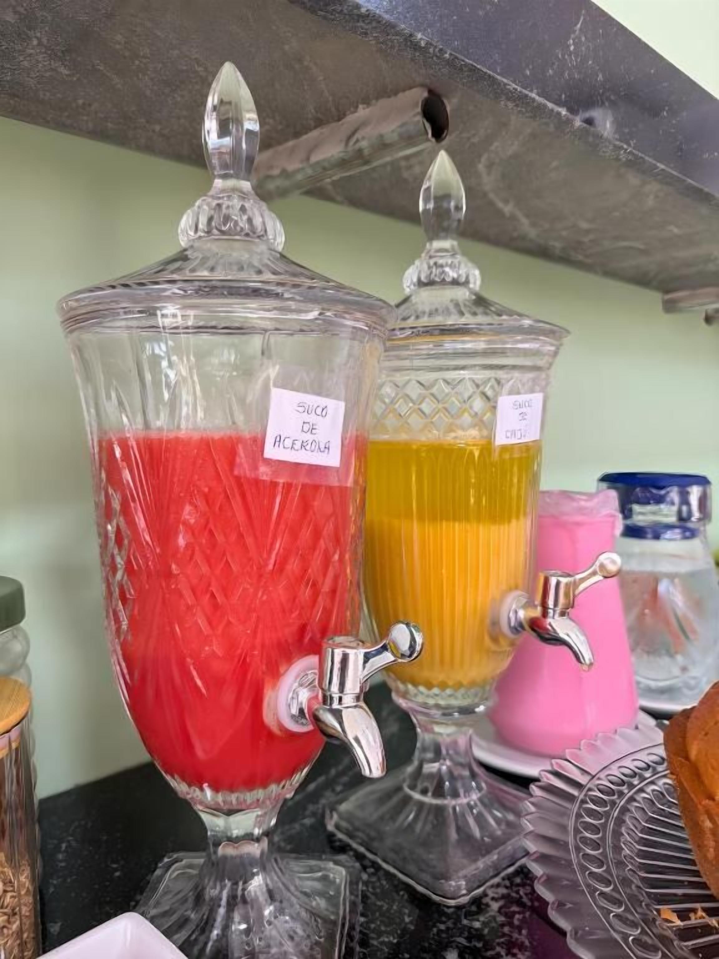 Two glass dispensers with taps, one labeled 'Suco de Açaí' and the other 'Suco de Açafrão'.