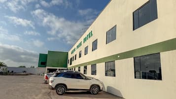 Hotel com fachada branca e detalhes verdes, um SUV estacionado e céu claro.