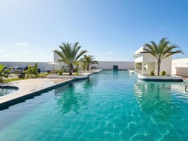 Una piscina con agua cristalina azul, rodeada de palmeras y un edificio blanco al fondo.