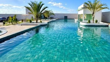 Una piscina con borde de baldosas, palmeras y un edificio moderno al fondo.