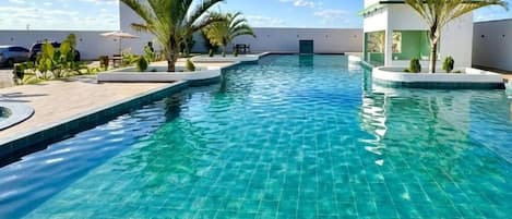 A swimming pool with a tiled deck, palm trees, and a modern building in the background.