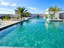 Una piscina con borde de baldosas, palmeras y un edificio moderno al fondo.