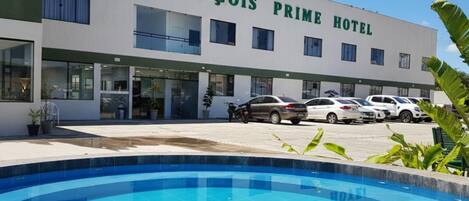 Hotel met een zwembad op de voorgrond, een parkeerplaats met meerdere auto's, en een gebouw met de naam 'LENÇOIS PRIME HOTEL' op de gevel.