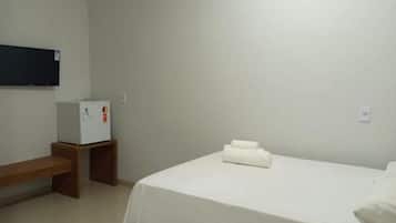 A hotel room with a bed, a small table, a bench, a wall-mounted TV, and a refrigerator.