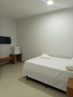 Habitación de hotel con cama, una mesita, un banco, un televisor de pared y un refrigerador.