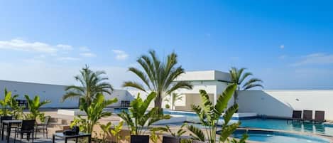 An outdoor seating area with tables and chairs, a pool, and palm trees.