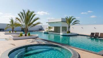 A swimming pool area with a circular hot tub, palm trees, and a modern building structure.