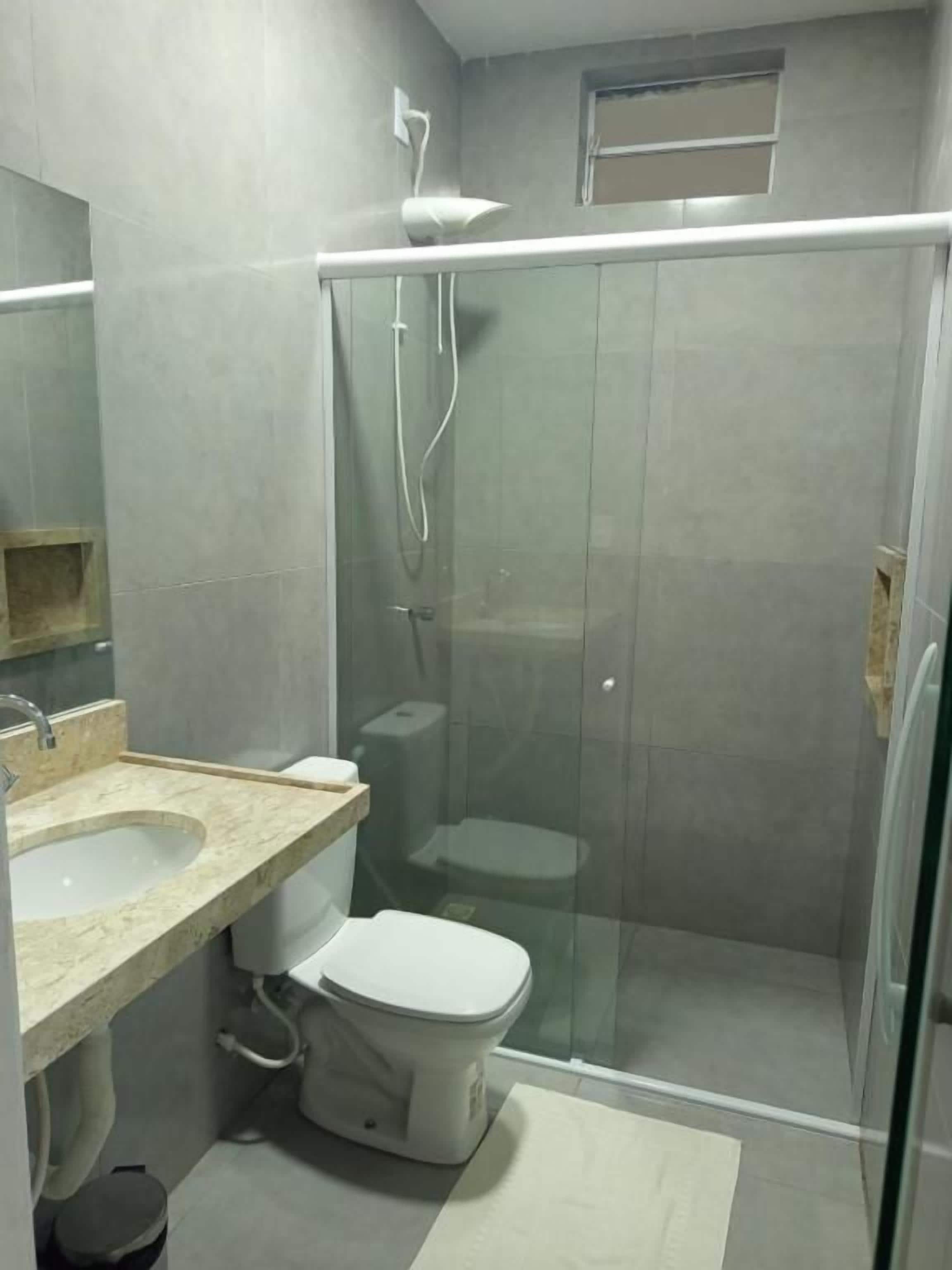 Un baño con ducha envuelta en cristal, inodoro y lavamanos con encimera.