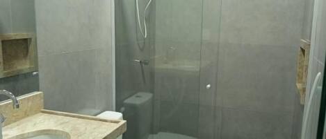 Un baño con ducha envuelta en cristal, inodoro y lavamanos con encimera.