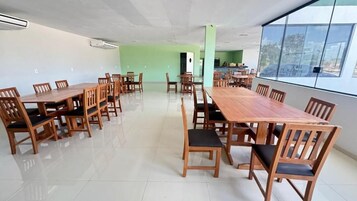 Un comedor amplio con varias mesas y sillas de madera, una pared de acento verde y ventanas grandes con vistas.