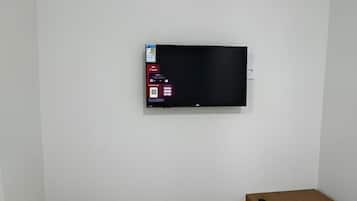 A room with a flat-screen TV mounted on the wall, a wooden bench, and a small white refrigerator.
